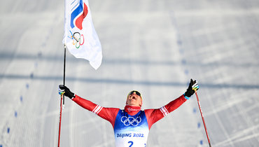 Александр Большунов финиширует с флагом на Олимпиаде в Пекине.