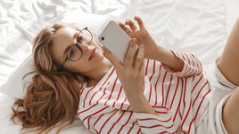 Девушка лежит на кровати и смотрит в телефон