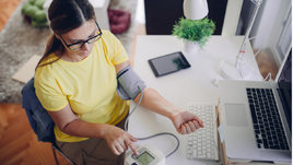 Женщина сидит за столом и измеряет давление