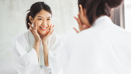 Красивая корейская девушка делает омолаживающий массаж лица напротив зеркала
