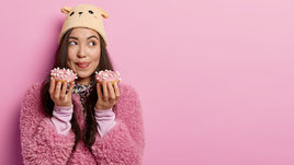 Молодая девушка ест сладкие пончики на розовом фоне