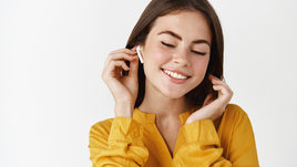 Молодая красивая девушка улыбается и слушает музыку в беспроводных наушниках