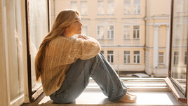 Молодая красивая девушка сидит на подоконнике и смотрит в даль