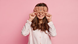 Красивая молодая девушка в маске для сна на розовом фоне