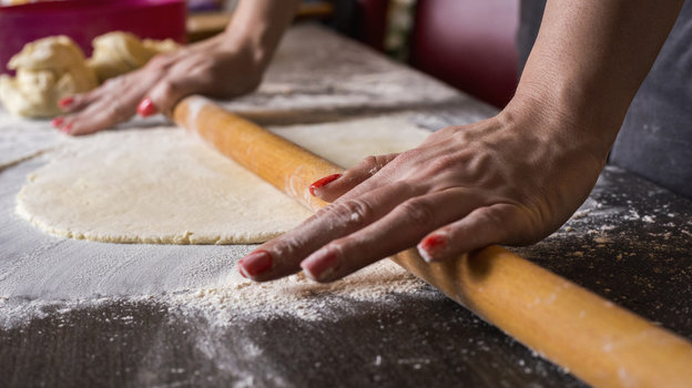 Девушка раскатывает тесто скалкой.