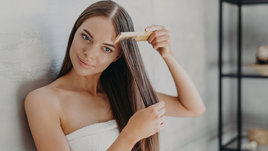 Молодая брюнетка расчесывает волосы гребнем после принятия душа и применения маски по уходу за волосами