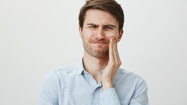 Мужчина держится за щеку из-за боли в зубах мудрости