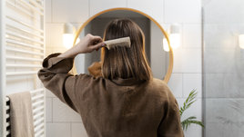 Девушка перед зеркалом расчесывает волосы и обнаружила первую седину