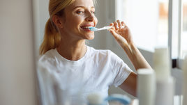 Женщина чистит зубы у зеркала.