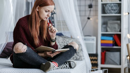 Девушка сидит с блокнотом и думает.