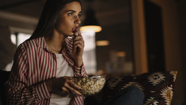 Девушка на диване в гостиной ест попкор