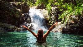 Девушка купается рядом с водопадом.