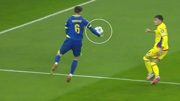 Мяч попадает в руку футболисту сборной Боснии Беньямину Тахировичу.