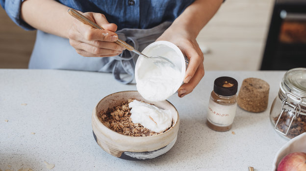 Женщина добавляет йогурт в мюсли