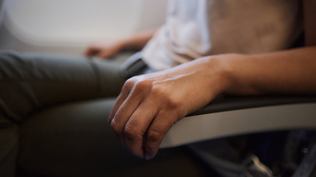 Мужские руки держат ручки сидения самолета