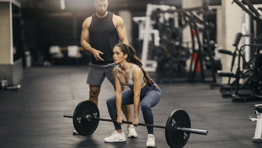 Девушка делает становую тягу под руководством тренера