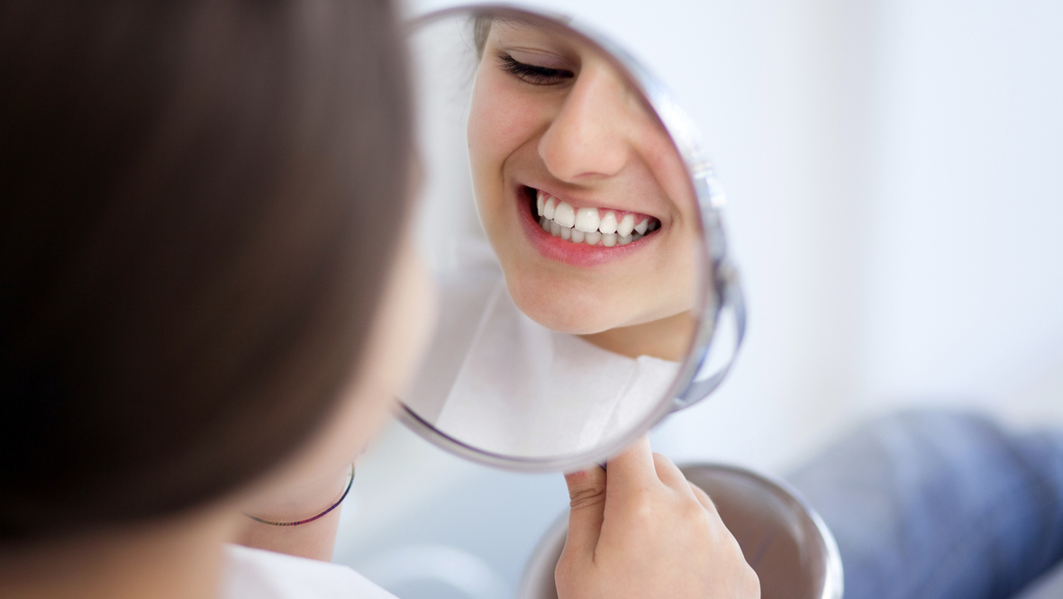 Девушка рассматривает зубы в зеркале