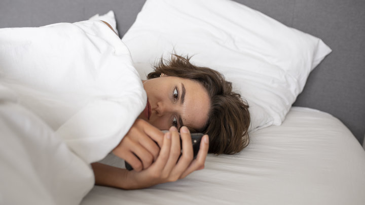 Девушка лежит в постели и смотрит в телефон
