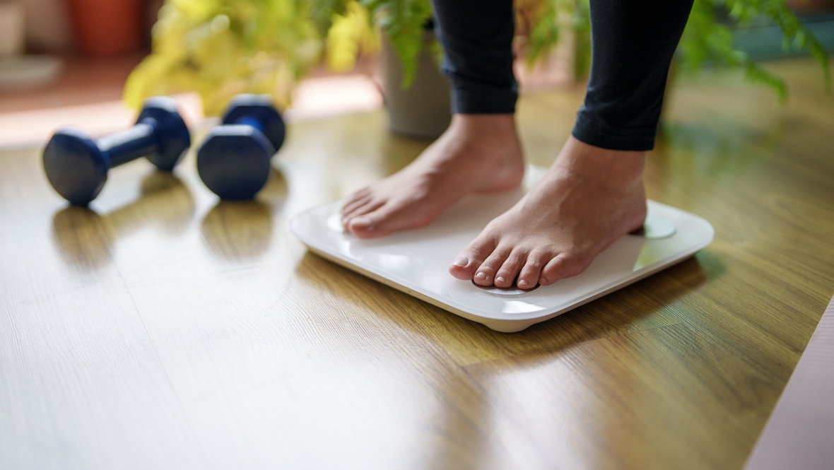 Девушка стоит на весах и рядом гантели